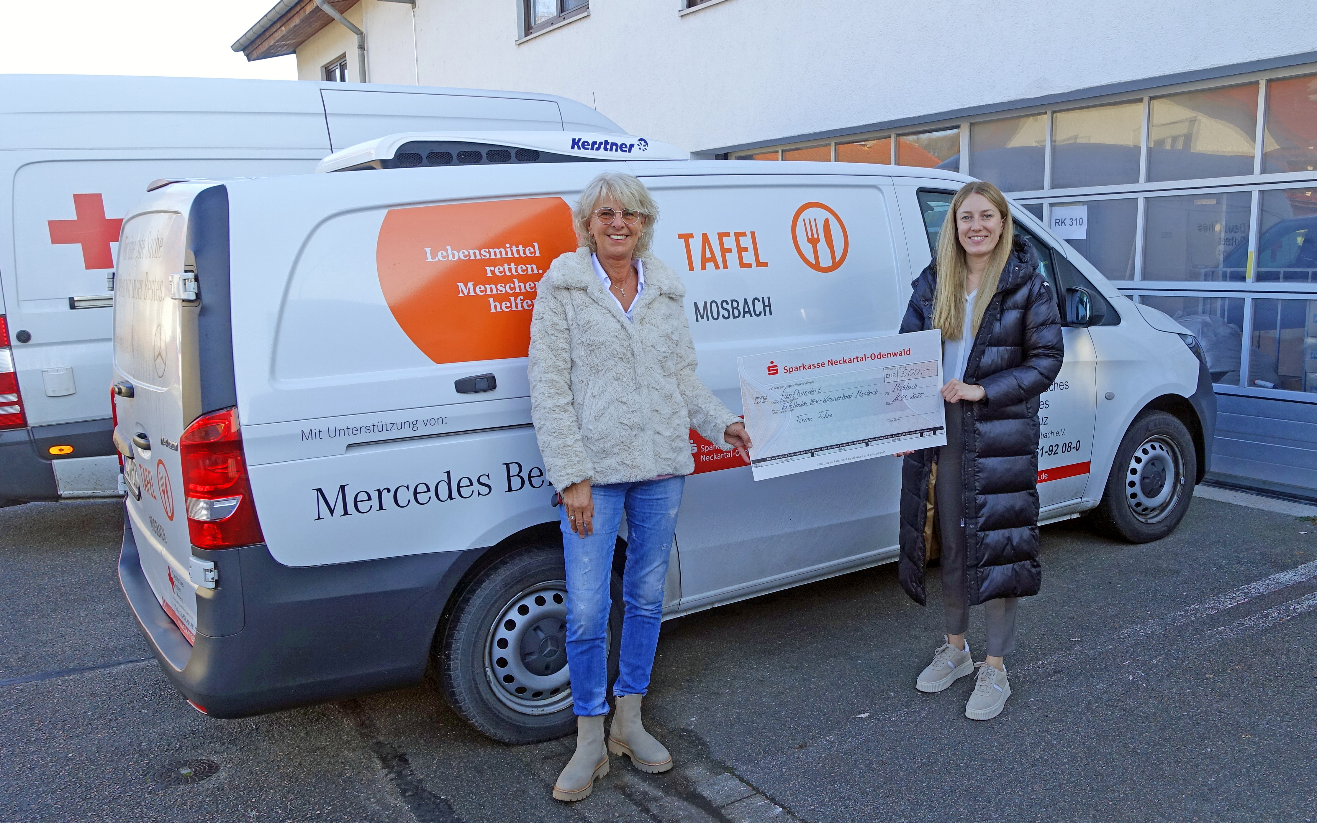 Vor dem Fahrzeug des Tafelladens halten Manuela Schönig vom Tafelladen und Janine Horn von FIBRO einen symbolischen Scheck über 500 Euro in den Händen.