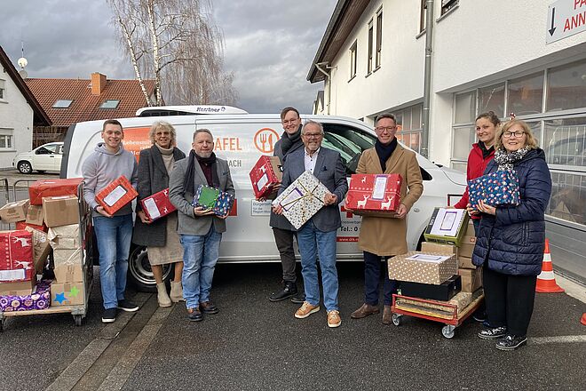 Das Bild zeigt Menschen vor einem Fahrzeug der Tafelladen. Sie halten einige der Päckchen, die gespendet wurden, in den Händen. Dabei sind Mosbachs OB Julian Stipp und DRK-Präsident Gerhard Lauth